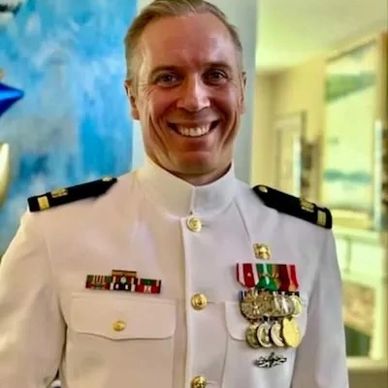 Smiling naval officer in a white uniform adorned with medals and ribbons.