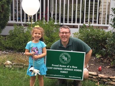 Girl and man posing with school sign in yard.