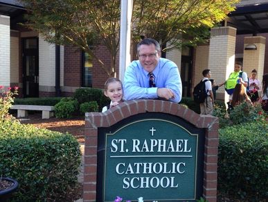 Man and child smiling behind a school sign.