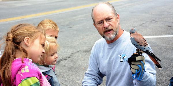Man showing a bird to three children outdoors on the street.
