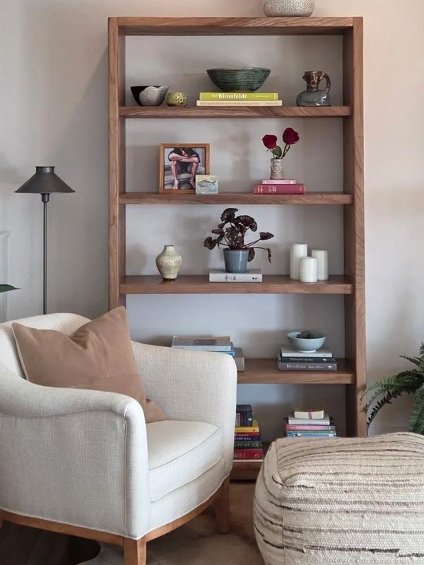 Cozy reading nook with a beige armchair, ottoman, and wooden bookshelf filled with books and decor.