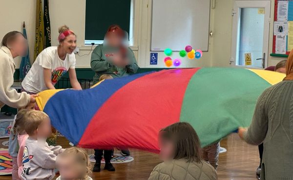 Children and adults playing with a colorful parachute indoors.
