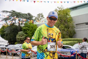 Man giving thumbs up during a colorful race event with cartoon-themed shirts.