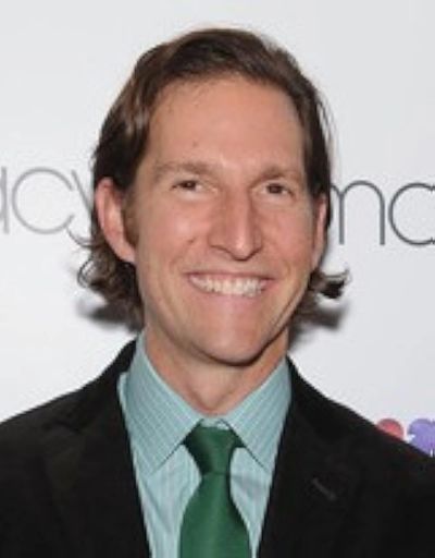 Smiling man in a suit and green tie posing at an event.