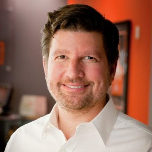 Smiling man with short brown hair wearing a white shirt.
