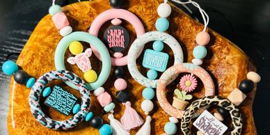 Colorful beaded baby pacifier clips with playful designs on a wooden surface.