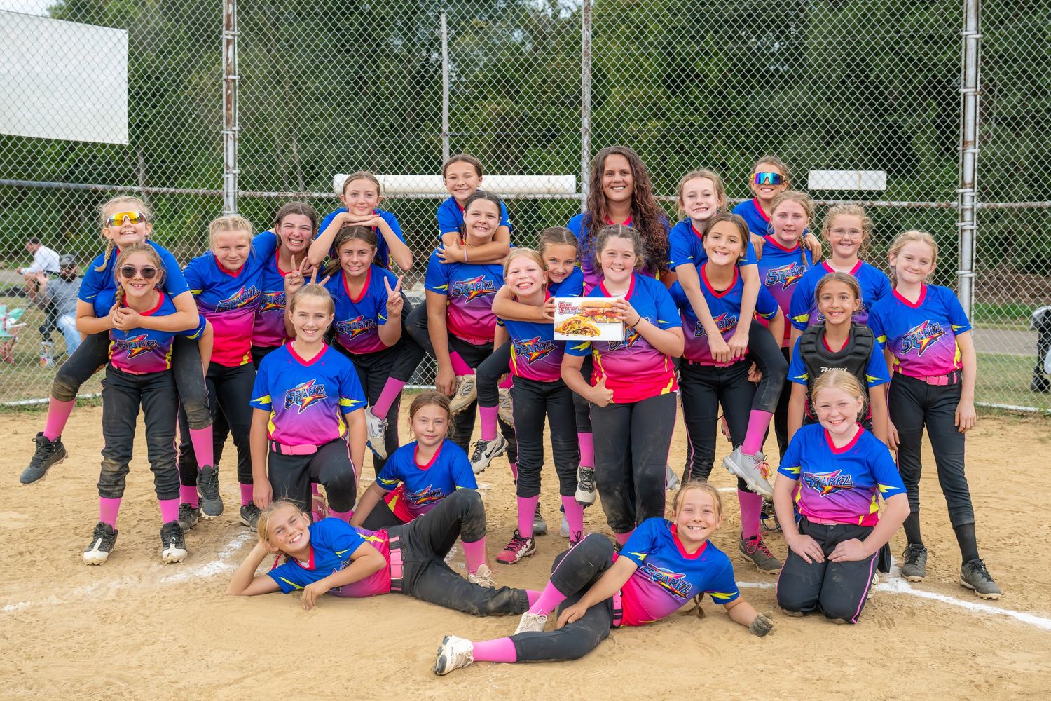 Youth softball team posing happily on the field in matching blue and pink uniforms.