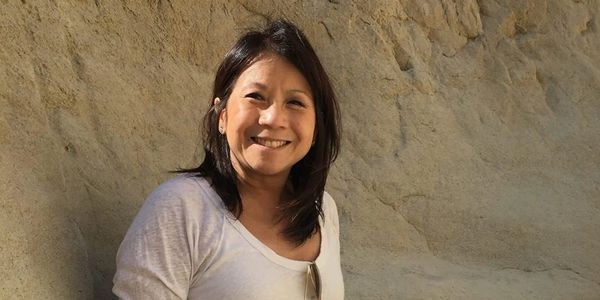 Woman smiling outdoors against a rock wall.