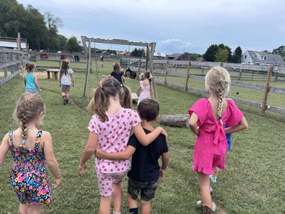 Children walk together on a grassy path near a fenced playground.