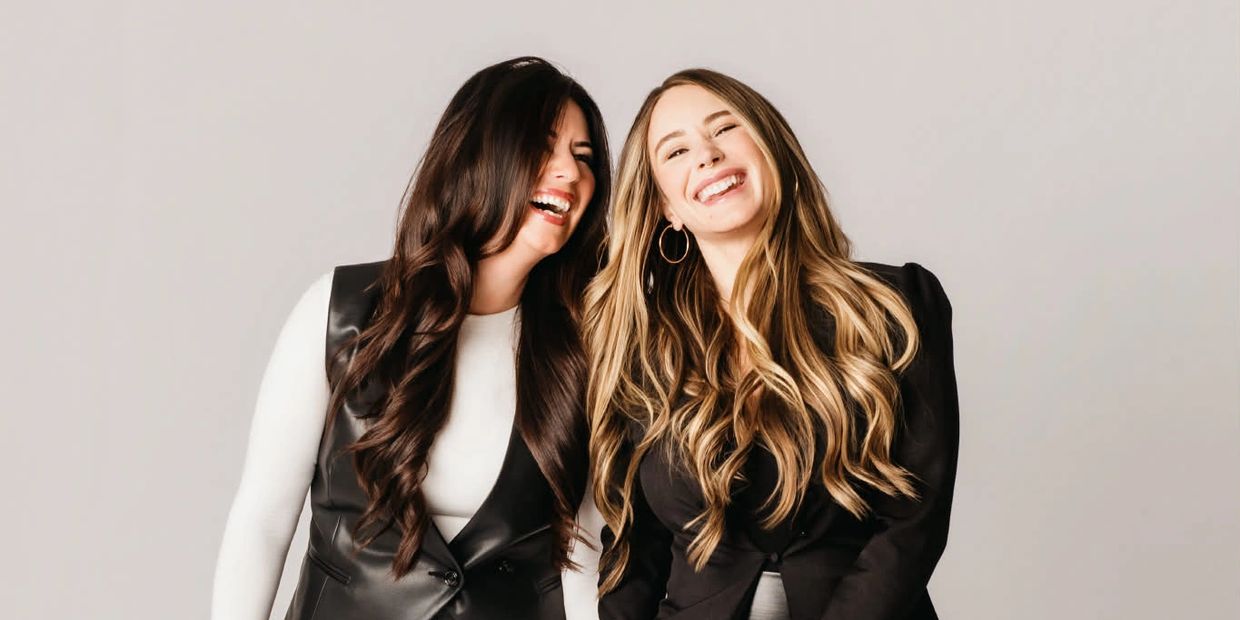Two women laughing joyfully, dressed in stylish black and white outfits.
