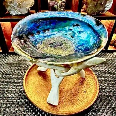A decorative blue and green bowl held by white hands on a wooden base.