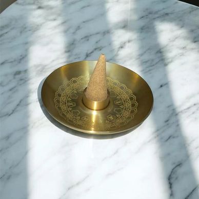 Brass incense holder with a cone-shaped incense on a marble surface.