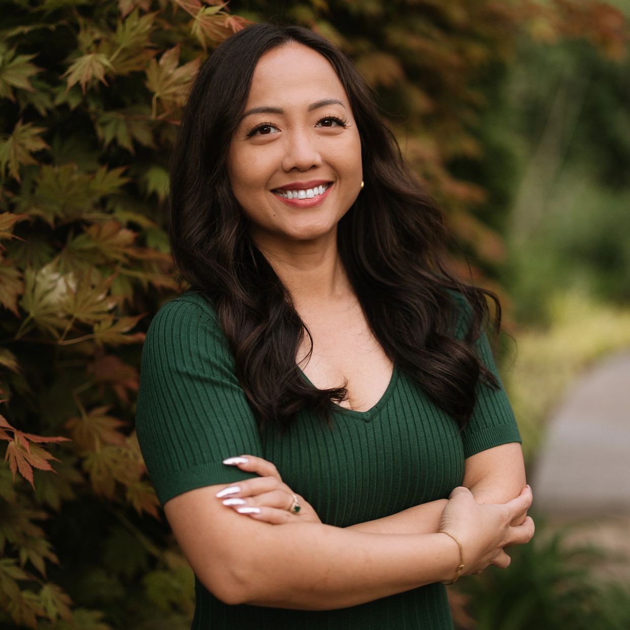 Smiling woman in green dress standing with arms crossed outdoors.