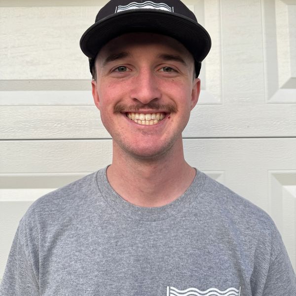 Smiling young man wearing a black cap and gray shirt with a logo.