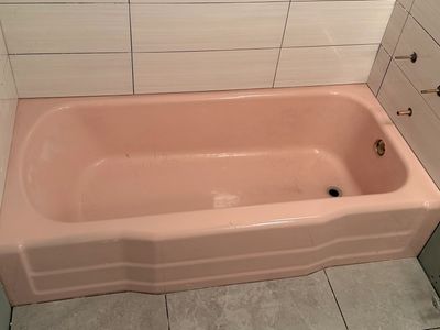 A partially tiled bathroom with a pink bathtub and green drywall.