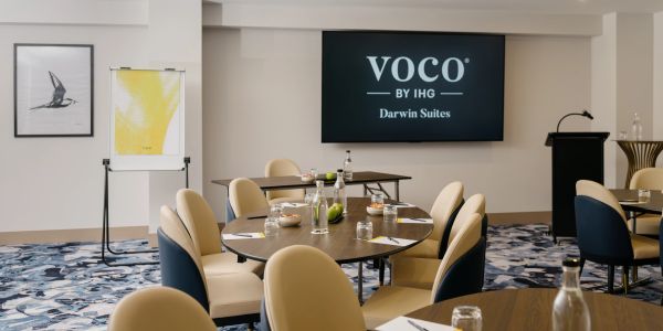 Modern conference room at Voco by IHG Darwin Suites with round tables and beige chairs.