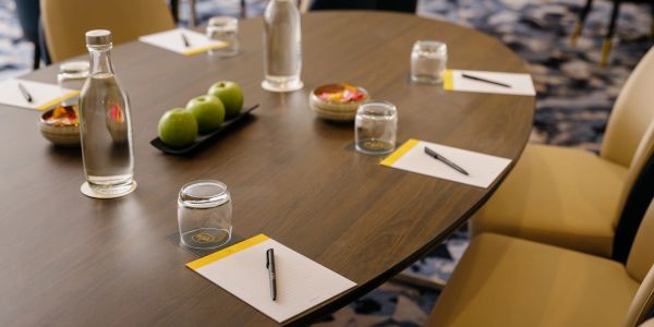 A neatly arranged meeting table with notepads, pens, water bottles, and green apples.
