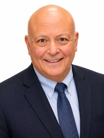 Smiling bald man in a navy suit and blue tie against a white background.