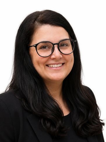 Smiling woman with black hair and glasses in a black blazer against white background.
