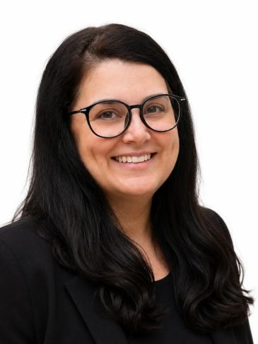 Smiling woman with black hair and glasses in a black blazer against white background.