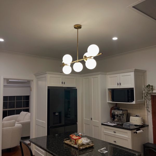 Modern kitchen with black granite island and white cabinetry under warm globe chandelier.