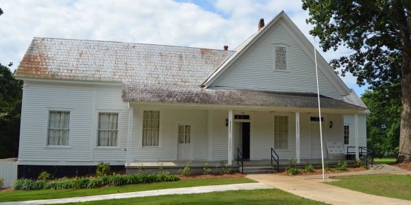 Historic white wooden house with a large porch and flagpole.