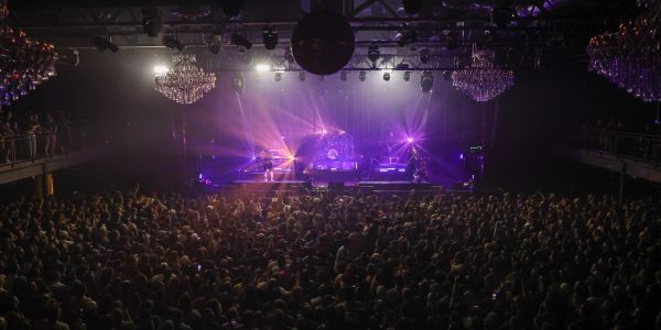Large crowd watching a concert with purple stage lights.