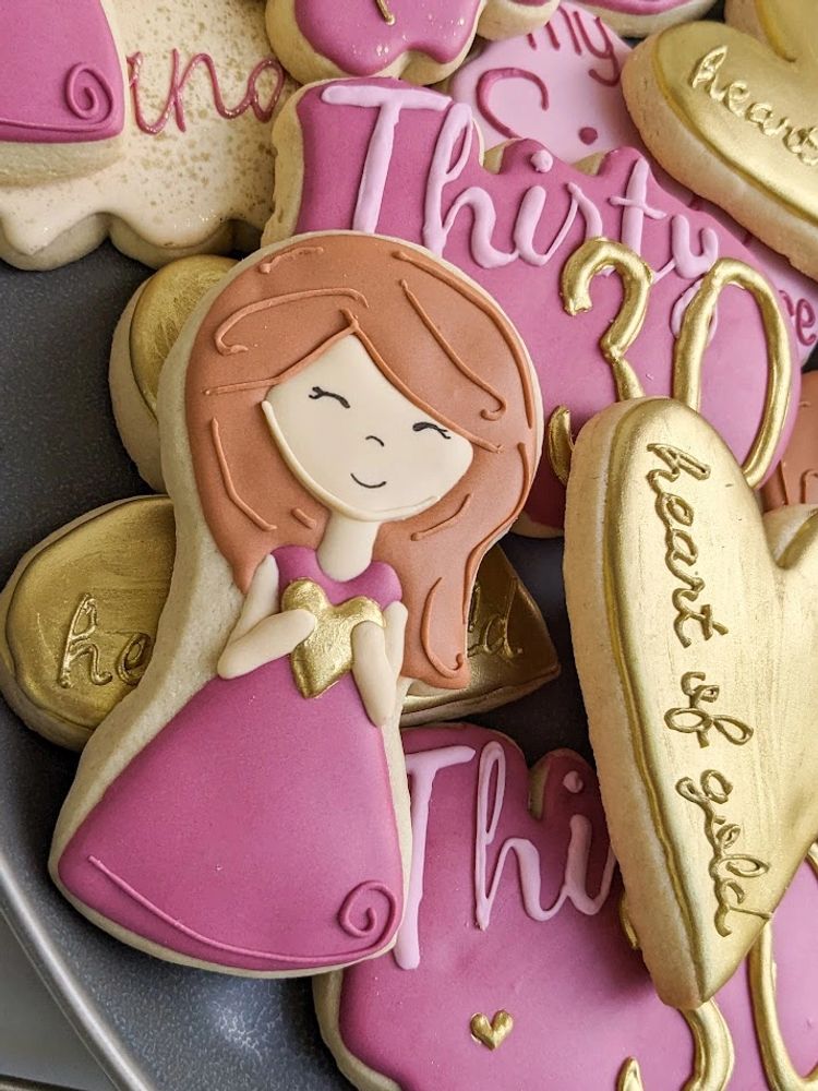 Sugar cookies on a platter, including a girl holding a gold heart, Thirty, and a large gold heart