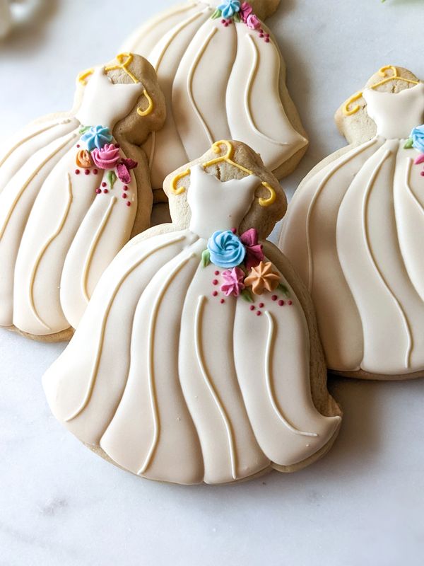 Sugar cookies shaped like wedding gowns  with an ivory tone and florals at the waist