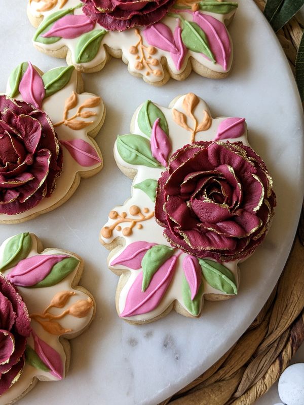 Sugar cookies shaped like roses with green, pink, and orange leaves