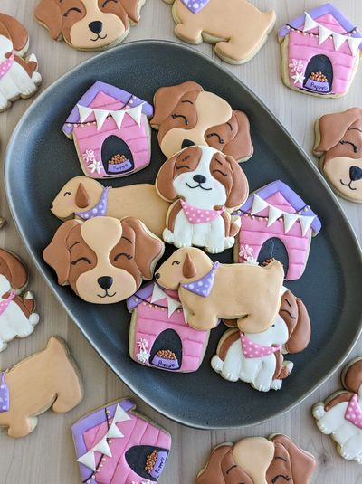 Puppy sugar cookies arranged on a dark platter, with other puppy sugar cookies surrounding it