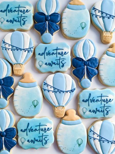 Baby shower sugar cookies with bottles, rattles, hot air balloons, and plaques with Adventure Begins