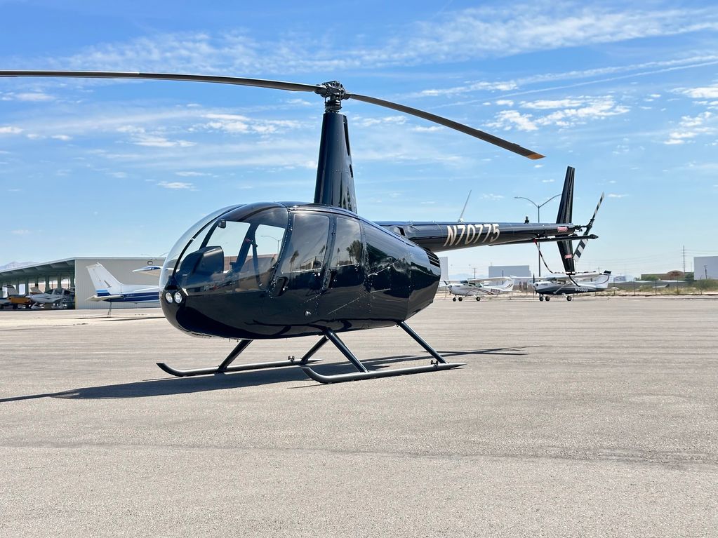 Black helicopter parked on airfield with blue sky.