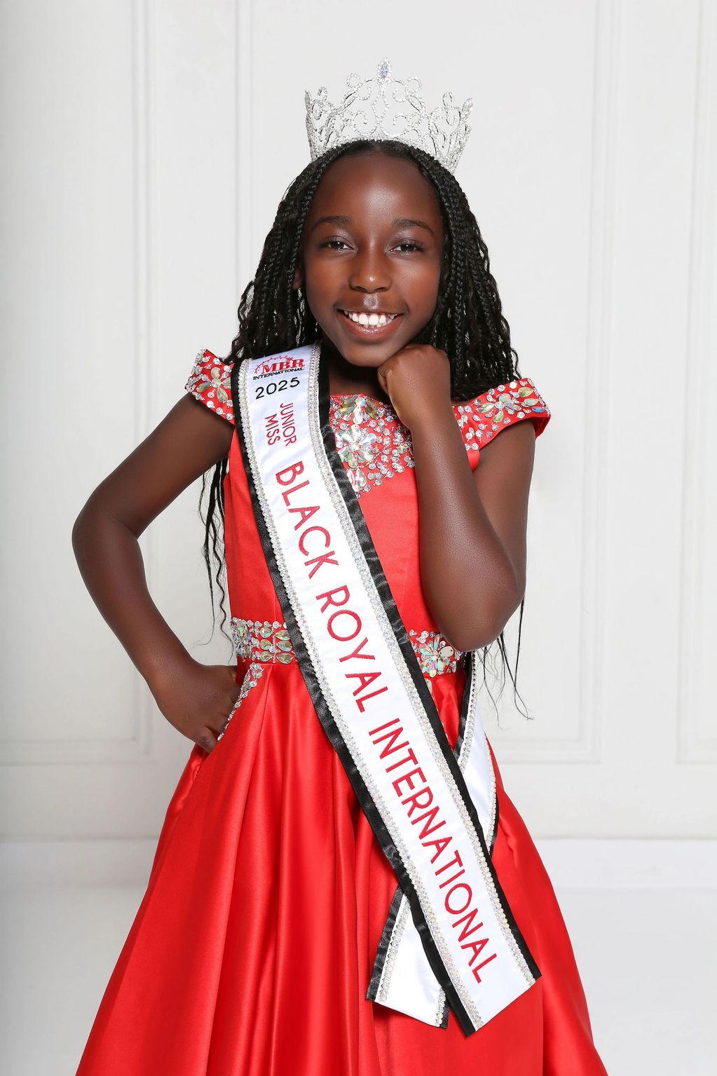 Young girl crowned in a red dress with a sash.