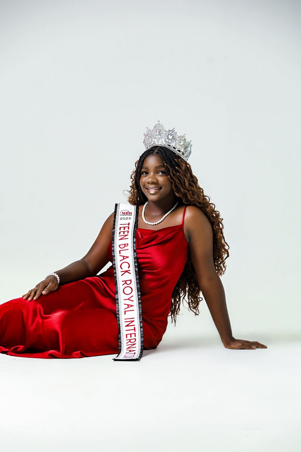 Young woman crowned Teen Black Royal International 2025 in red dress.