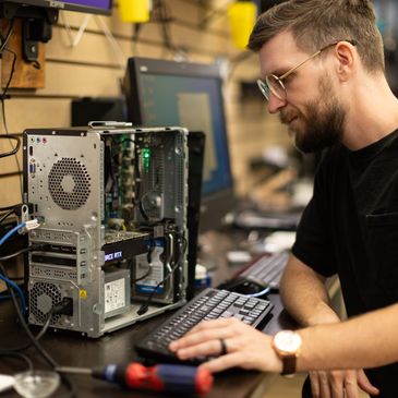 A technician smiling as he repairs and diagnoses a desktop computer.