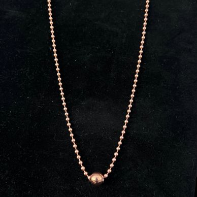 Rose gold beaded necklace with a central polished bead on a black background.