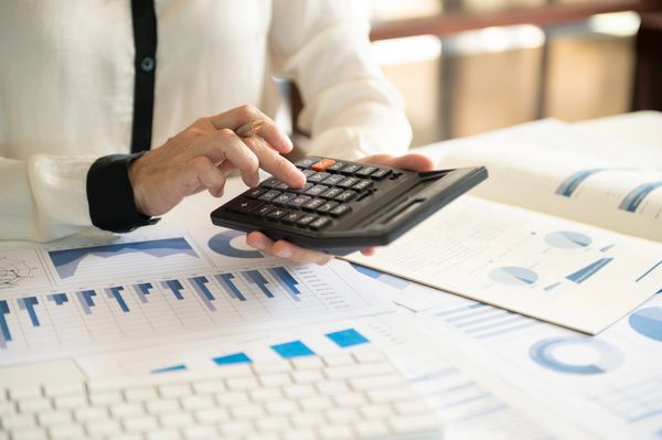 Person uses a calculator with financial charts and a keyboard on the desk.