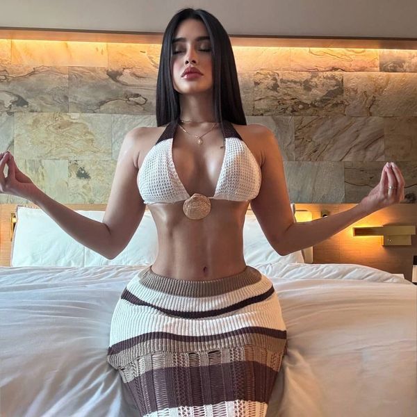 Woman meditating on a bed in a stylish outfit with eyes closed.