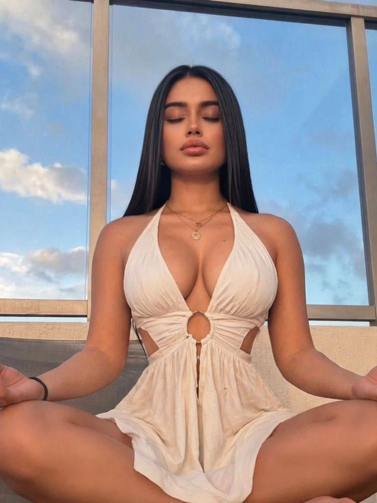 Woman meditating outdoors in white dress with serene expression.