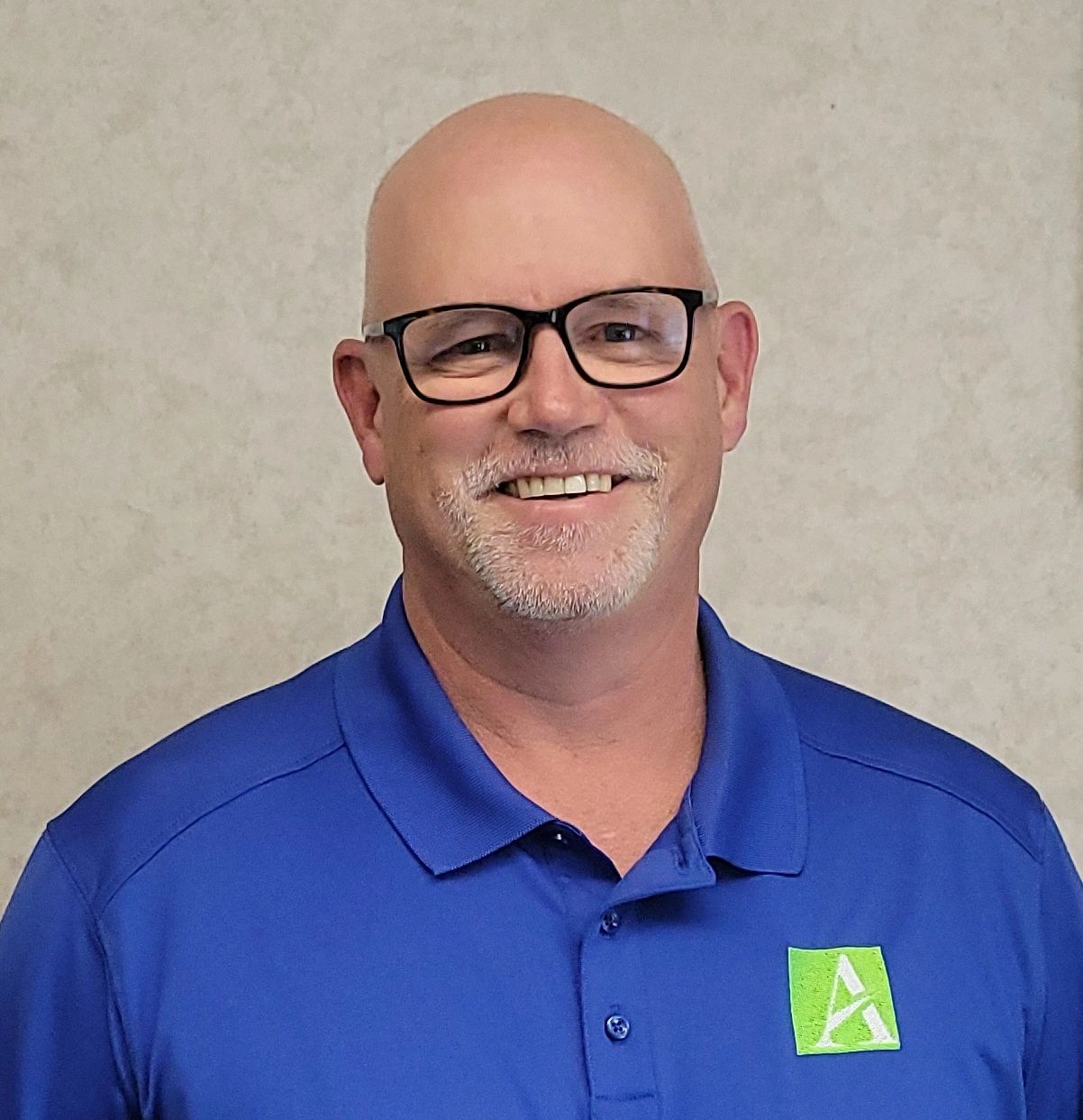 Smiling bald man in glasses and blue polo shirt.