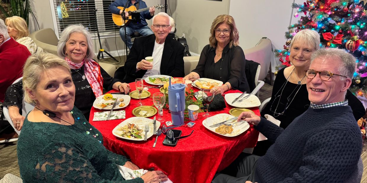 Group of people enjoying a festive meal around a decorated table with a Christmas tree.