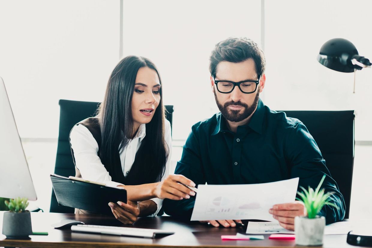 Two professionals reviewing documents together in a modern office setting.