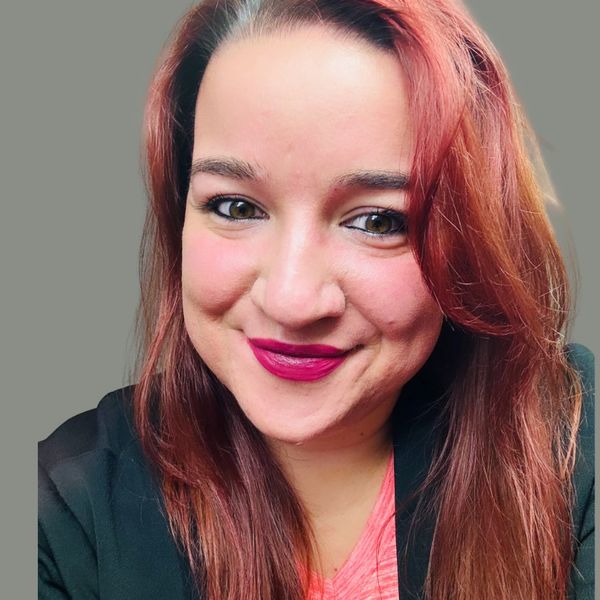 Close-up portrait of a smiling woman with red hair and bright lipstick.