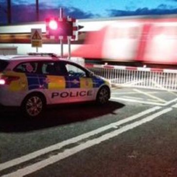 Police car parked near railway crossing at night with train passing by.