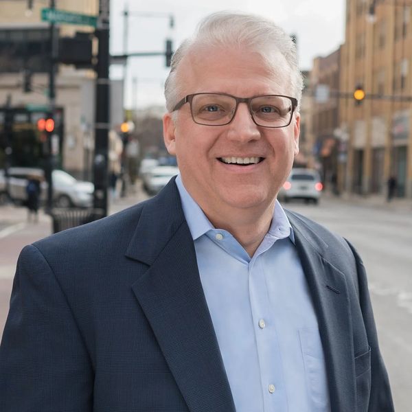 Smiling man in glasses and suit jacket outdoors.