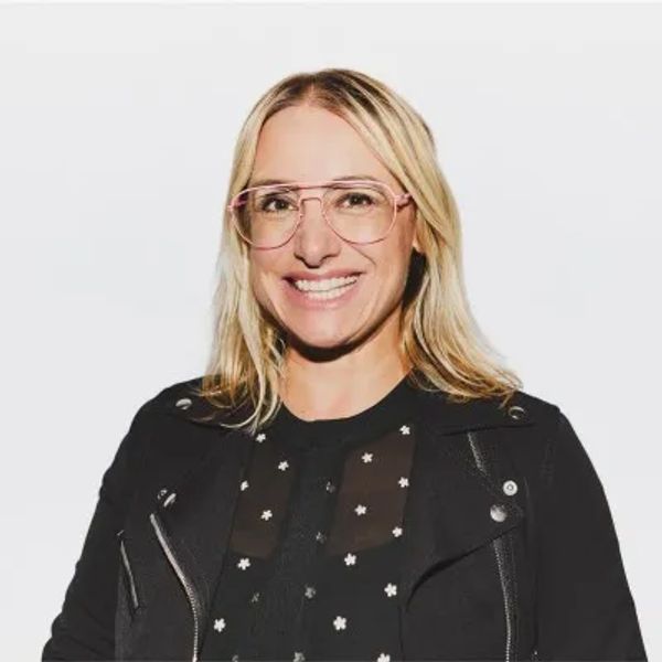 Smiling woman with glasses and blonde hair in casual black outfit.