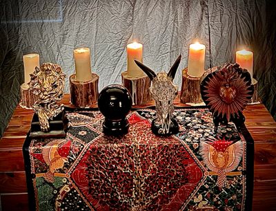 Mystical altar with candles and animal skulls on a patterned cloth.