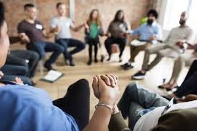 Group of people sitting in a circle holding hands, engaged in a support meeting.