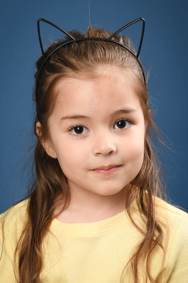 Young girl with cat ear headband and yellow shirt against blue background.
